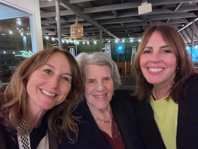 Three women, smiling, wearing black jackets.