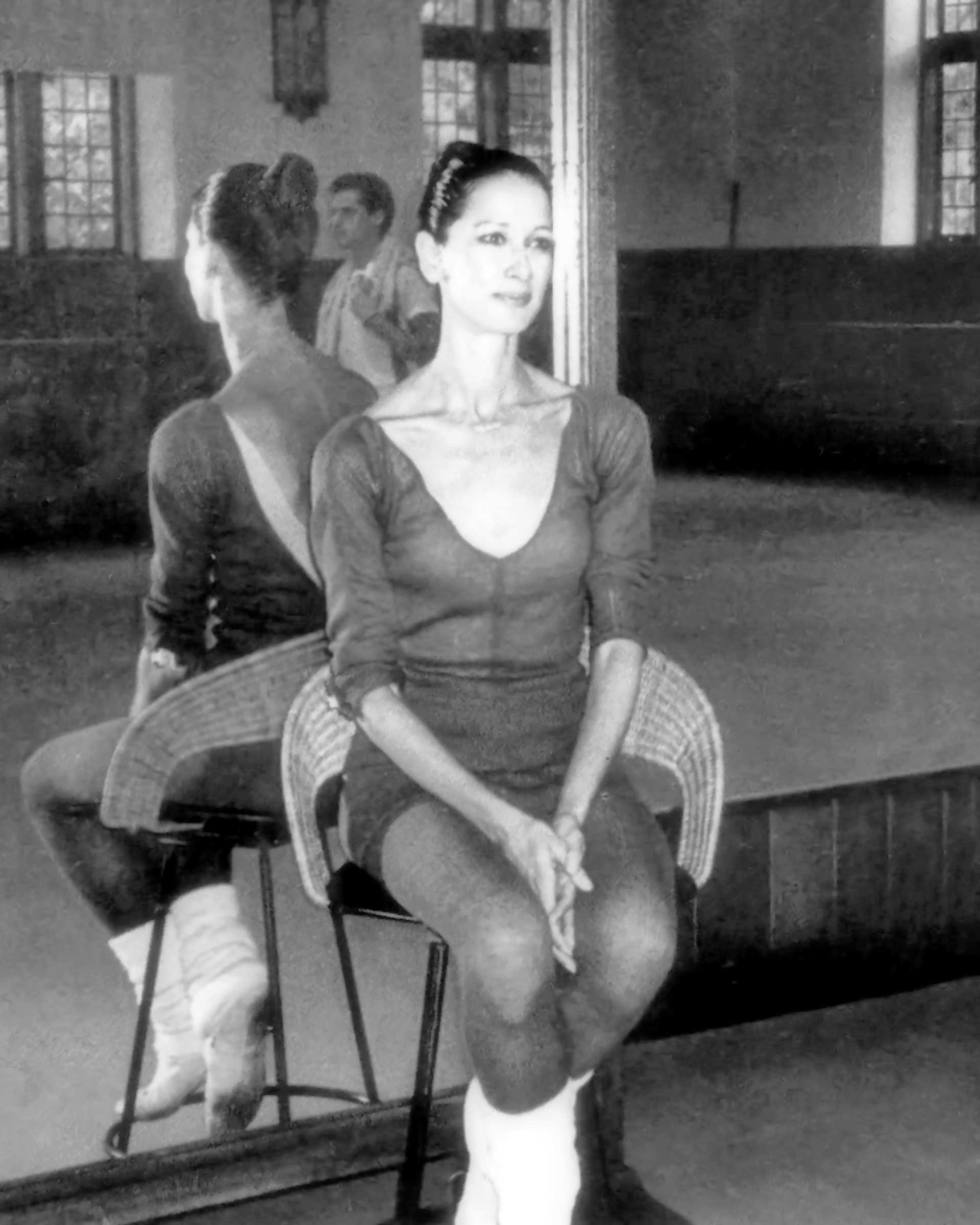 Dancer sitting on a stool in a dance studio in front of a mirror.