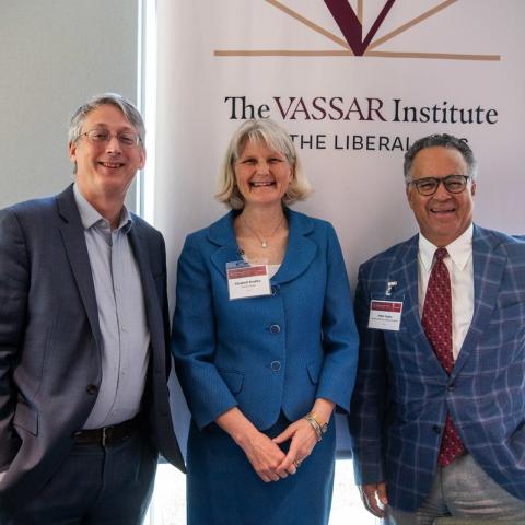 Three people stand in front of a banner that says “The Vassar Institute for the Liberal Arts”. President Elizabeth Bradley, a person with short gray hair and a blue dress, stands between a person with gray hair and a gray suit and a person with gray hair and a blue checked suit.