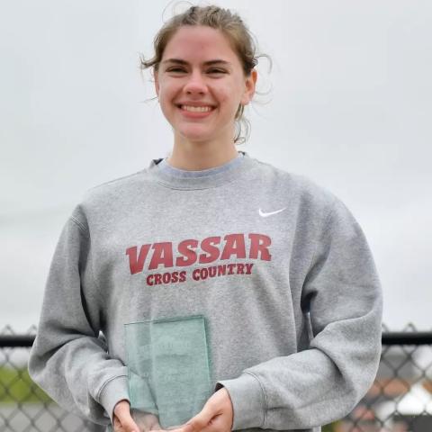 Smiling athlete with a Vassar Cross Country sweatshirt holding a tropy.